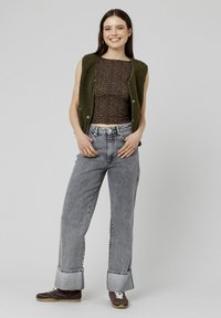 Gilet sans manches vert olive sur un top à imprimé léopard marron, associé à un pantalon en denim taille haute gris clair et des baskets marron.