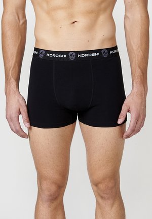 Boxer de algodón negro con diseño ajustado, que presenta una cinturilla elástica de marca con un patrón de calaveras. Textura suave, sin costuras visibles.