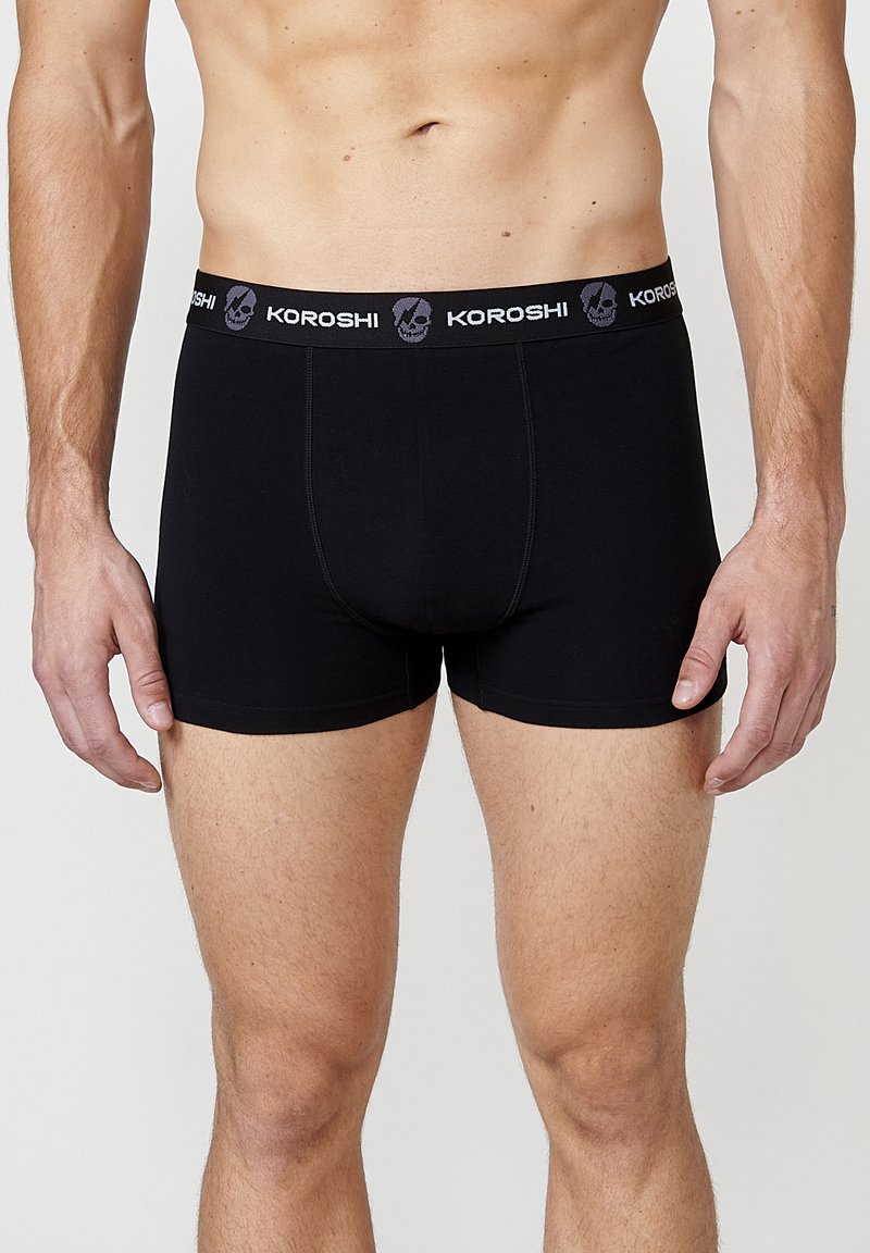 Schwarze Baumwollboxershorts mit tailliertem Schnitt, ausgestattet mit einem markenbedruckten elastischen Bund mit Totenkopf-Muster. Glatte Textur, keine sichtbaren Nähte.