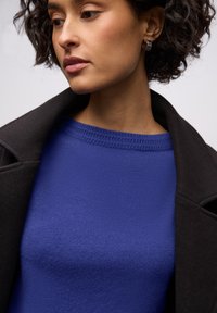 Gebreide trui in levendig blauw met een gestructureerde ronde hals, gecombineerd met een zwarte jas met een gevormde kraag.