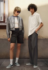 Metalická strieborná bomber bunda, biele crop top, čierne denimové šortky, šedé široké nohavice a kockované slip-on topánky.