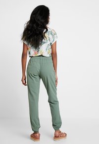 Joggers à taille élastique vert clair avec chevilles fuselées ; assortis à une chemise à manches courtes à motif floral dans des couleurs tamisées.