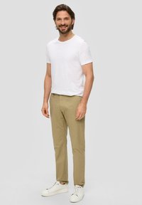 Beżowe chinosy z bocznymi kieszeniami, zestawione z dopasowanym białym t-shirtem i białymi sneakersami. Casualowy wygląd o minimalistycznym designie i czystych liniach.
