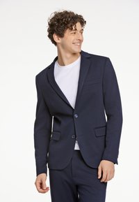 Blazer azul marino hecho de tela texturizada, con solapa muesca, cierre de dos botones y dos bolsillos frontales, usado sobre una camisa blanca.