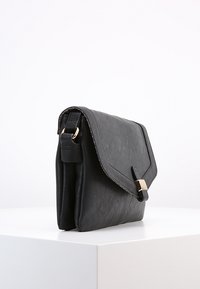 Borsa a tracolla nera in pelle con fibbia dorata e tracolla regolabile, esposta su una superficie bianca contro uno sfondo semplice.