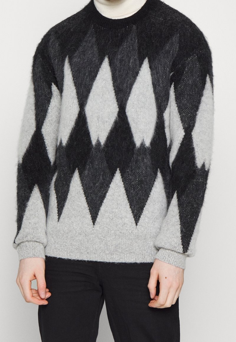 Stickad tröja i grått, svart och vitt, med ett diamantmönster. Mjuk textur, ribbade muddar och rund halsringning.