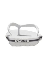 Des tongs blanches Crocs avec une semelle plate, des fines brides et un semelle intérieure texturée. Présente une bande noire et un logo "crocs" à l'arrière.