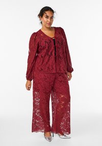 Ensemble en dentelle bourgogne comprenant un haut à manches longues avec des motifs floraux et un décolleté en V profond, associé à un pantalon large assorti.