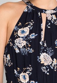 Vestido floral marino con escote en forma de lágrima, presenta flores en tonos azul claro y crema, textura plisada y un diseño de tirantes estilo halter.