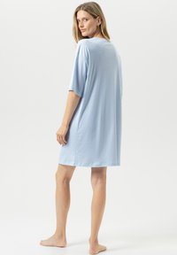 Niebieska, jasnoniebieska koszula nocna w paski, z krótkimi rękawami, luźnym krojem, długości do kolan, z miękkiego materiału, z okrągłym dekoltem. Widok od tyłu.