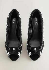 Pumps open-toe in velluto nero con decorazioni in strass e dettagli testurizzati. Forma arrotondata con un rivestimento interno liscio.