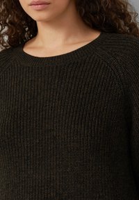 Dunkelgrüner Strickpullover mit rundem Halsausschnitt und strukturiertem Rippmuster, ausgestattet mit Raglanärmeln und einem weichen, dickeren Stoff.