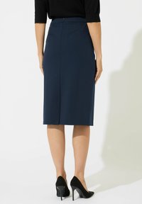 Marineblauer, taillierter Bleistiftrock mit Hinterfalte, flachem Bund und glatter Textur. Kombiniert mit schwarzen High-Heels.