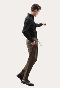 Maglietta nera a maniche lunghe abbinata a pantaloni marroni con vita con coulisse, taglio dritto e tasche, completata da scarpe nere.