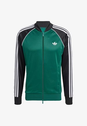 Grüne und schwarze Zip-Jacke mit weißen Drei-Streifen-Akzenten, gerippten Bündchen und einem kleinen Logo auf der linken Brust. Glatte Textur.