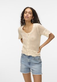 Gilet en tricot crème, avec des manches courtes, un col rond et une fermeture à boutons. Motif texturé avec un détail en bordure festonné.