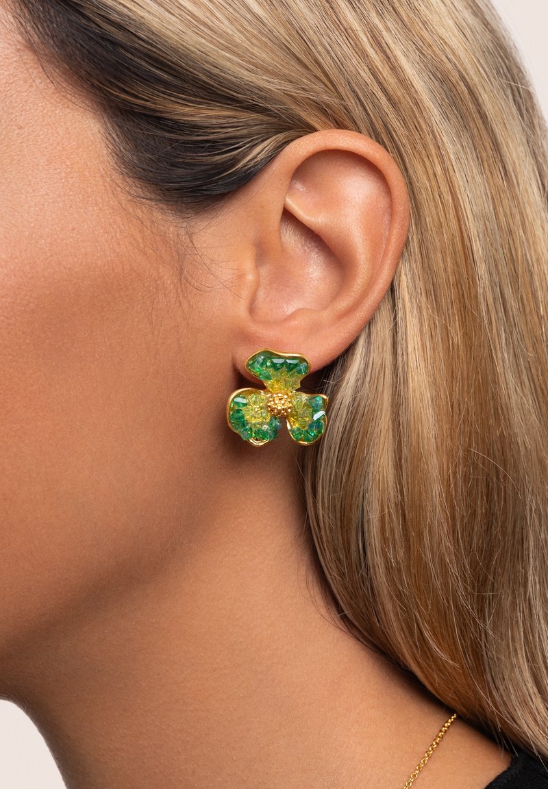 Orecchini floreali verdi realizzati in resina con base dorata; presentano petali texturizzati e un centro rotondo, indossati all'orecchio di un modello.