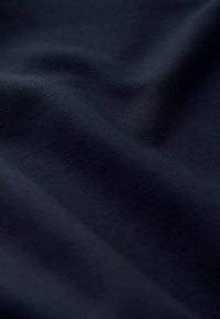 Marineblauer Stoff mit glatter Textur, der sanfte Wellen und Falten zeigt, wodurch das weiche, dehnbare Material und die tiefen Farben hervorgehoben werden.