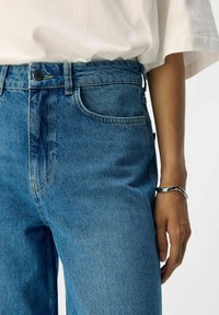 Svetlo modri traper hlače z visokim pasom, kontrastnim rumenim šivom in klasičnim pet-pocket oblikovanjem. Gladek material, rahlo zbledel.