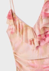 Gros plan d'une robe tie-dye rose et beige avec des fines bretelles et des volants superposés le long du décolleté.