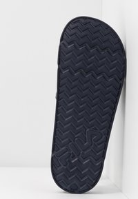 Svart gummisko sula med ett zigzag-mönster och logotype. Kanten är rundad, med en texturerad yta för grepp och hållbarhet.
