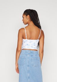 Top corto blanco con estampado floral en azul claro, con tirantes delgados ajustables. Combinado con una falda de mezclilla azul claro de cintura alta.
