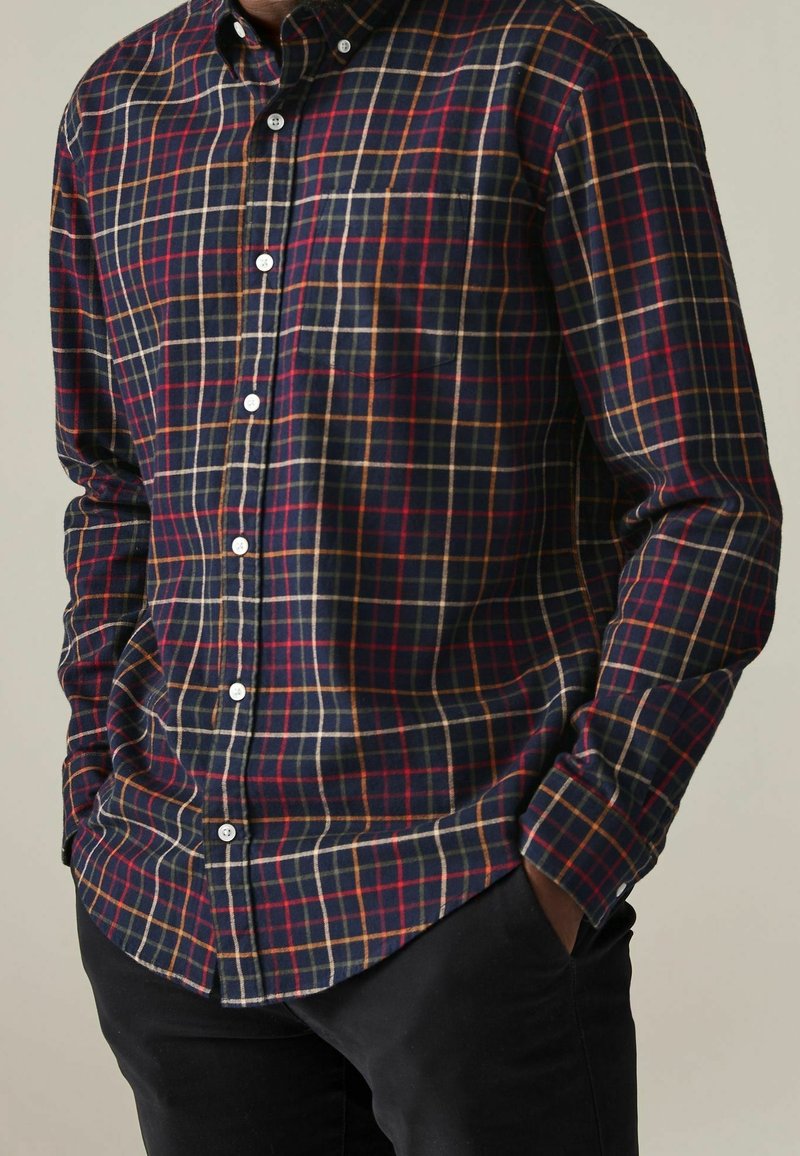 Camicia a quadri blu navy con controlli rossi e beige; presenta un colletto con bottoni, maniche lunghe e una tasca sul petto. Tessuto in cotone.