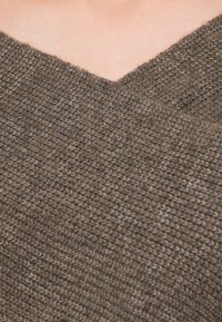 Brun strikket genser med V-hals design. Teksturen ser myk og chunky ut, og viser et vevd mønster og varierte brune nyanser.