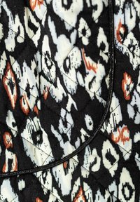 Gepolsterter Stoff mit einem schwarz-weißen Design und orange-roten Akzenten. Die Textur ist glatt und mit einem schwarzen Randdetail umrandet.
