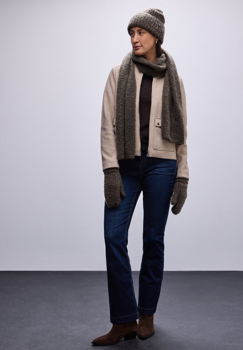 Giacca beige, maglione scuro, jeans blu scuro. Cappello di lana grigia, sciarpa e guanti. Stivali con tacco marroni. Texture morbide, vestibilità informale.