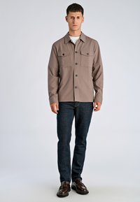 Bruine overhemd met knopen, twee borstzakken, lange mouwen en een overhemdkraag, gecombineerd met donkerblauwe spijkerbroek en bruine schoenen.