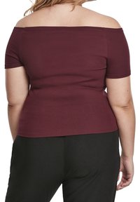 Burgundy, žebrovaný top s odhalenými rameny a krátkými rukávy; přiléhavý střih. Spárováno s černými kalhotami, které mají hladkou strukturu.