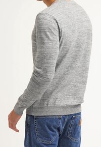Pull gris en maille avec manches longues, ourlet côtelé et texture douce, associé à un jean en denim bleu. Coupe décontractée, vue de dos.