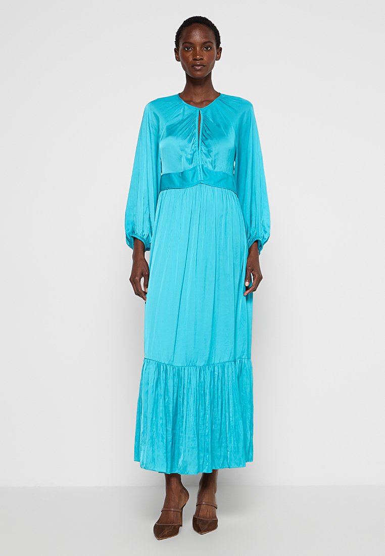 Ein langes, türkisfarbenes Satin-Kleid mit puffigen Ärmeln, elastischem Taillenbund und einem gestuften, gefältelten Saum. Schlüssel-Ausschnitt am Ausschnitt.