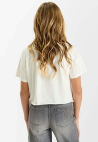 T-shirt blanche, coupée, à manches courtes, associée à un jean gris délavé taille haute avec des poches arrière ornées de surpiqûres.