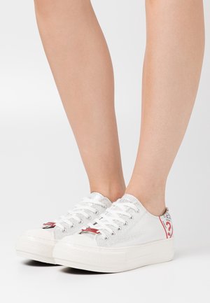 Feet wearing white low-top platform sneakers with white laces and a red question mark design on the heel area.