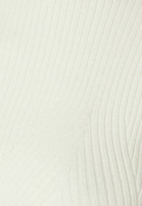 Krémová ribrová pletenina s vertikálními liniemi a jemnou strukturou, která se vyznačuje mírným leskem a nenápadnou variabilitou tloušťky.