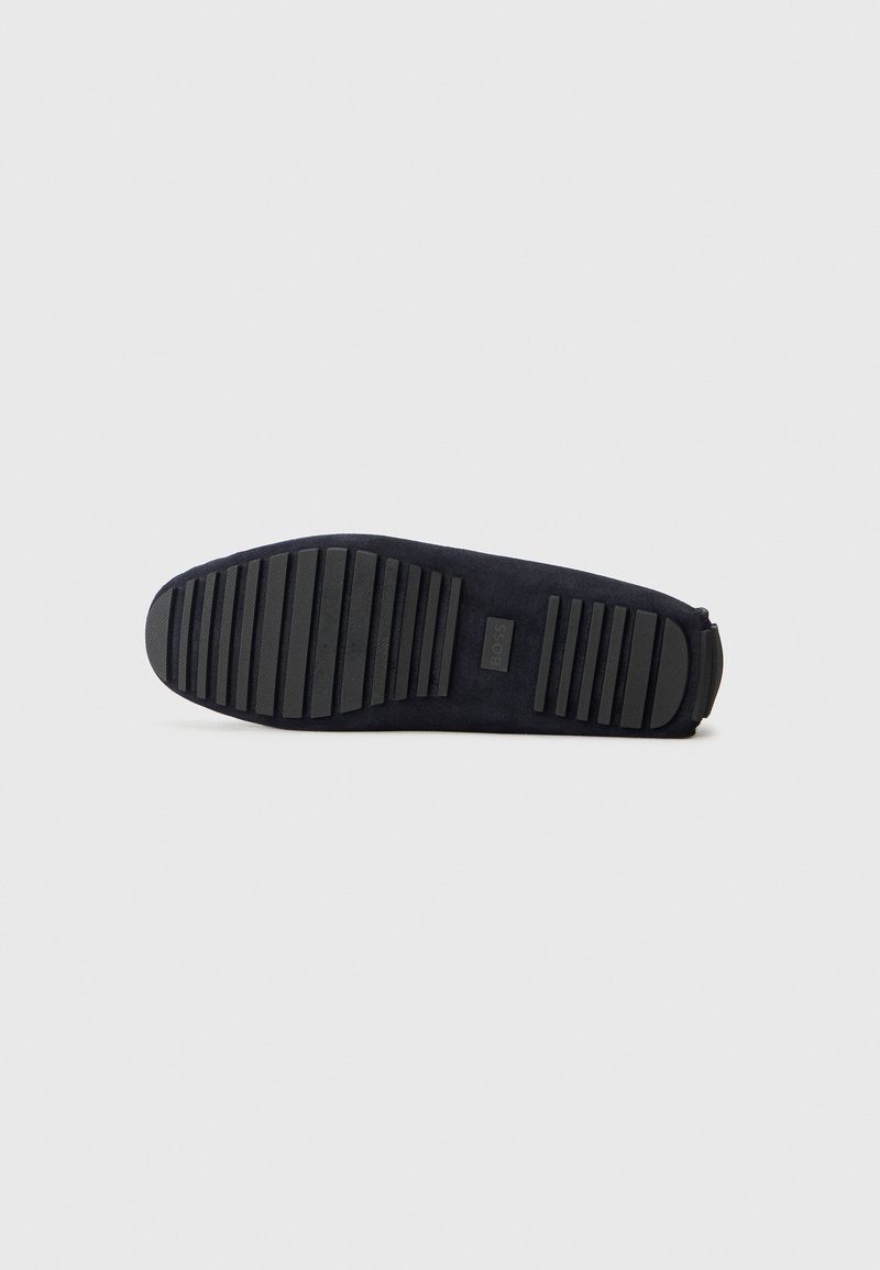 Sole of black shoe with deep horizontal grooves and rubber grip, featuring a small rectangular logo in the center.