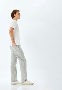 Jeans grises con un diseño de pierna recta, que presentan un ligero efecto desgastado, combinados con una camiseta blanca de manga corta y zapatillas blancas.
