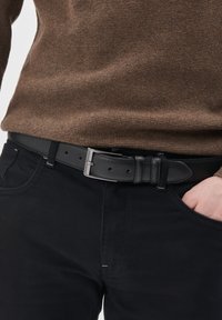 Fekete bőr öv ezüst fém csattal, t�öbb állítással ellátott lyukkal, sötét nadrág felett viselve, amit egy barna texturált pulóver egészít ki.