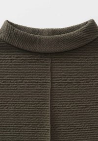 Tessuto khaki strutturato con un motivo a coste, caratterizzato da un colletto alto e dettagli con cuciture verticali. Texture liscia e morbida.