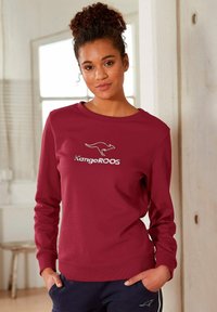 Weinrotes Sweatshirt mit langen Ärmeln, rundem Halsausschnitt und "KangaROOS"-Logo. Weicher Stoff mit gerippten Bündchen und Saum. Lässiger Schnitt und glatte Textur.