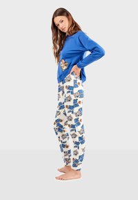 Top bleu à manches longues avec un graphique de dessin animé, associé à un pantalon de pyjama blanc imprimé de personnages colorés et de texte. Coupe décontractée, tissu doux.