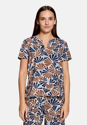 Femme portant un haut à manches courtes assorti et un pantalon avec un motif en forme d’éventail marron, marine et bleu clair sur un fond clair.