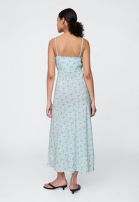 Svetlo modra cvetlična obleka s tankimi trakovi, tekočo silhueto in dolžino do kolen. Na tkanini so majhni rožnati cvetlični vzorci.