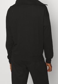 Sweatshirt noir avec un col montant, des manches longues et des poignets et un ourlet côtelés. Le tissu a une texture lisse et une coupe décontractée.