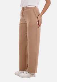 Pantaloni della tuta beige con vita regolabile, tasche laterali e una vestibilità rilassata. Realizzati in tessuto morbido, presentano un design a gamba dritta.