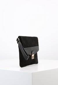 Svart mocka crossbody-väska med lock i slät läder, guldspänne och justerbar rem. Har en rektangulär form och en minimalistisk design.