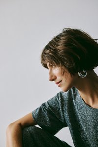 Szürke, textúrált ruhadarab rövid ujjakkal; nagy, kör alakú ezüst fülbevalók; lágy világítás, amely megvilágítja az arc vonásait és profilját.