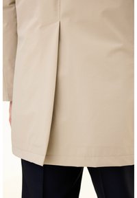 Beige trench coat with a straight cut, featuring a vent at the back and contrasting stitching. The texture appears smooth and lightweight.